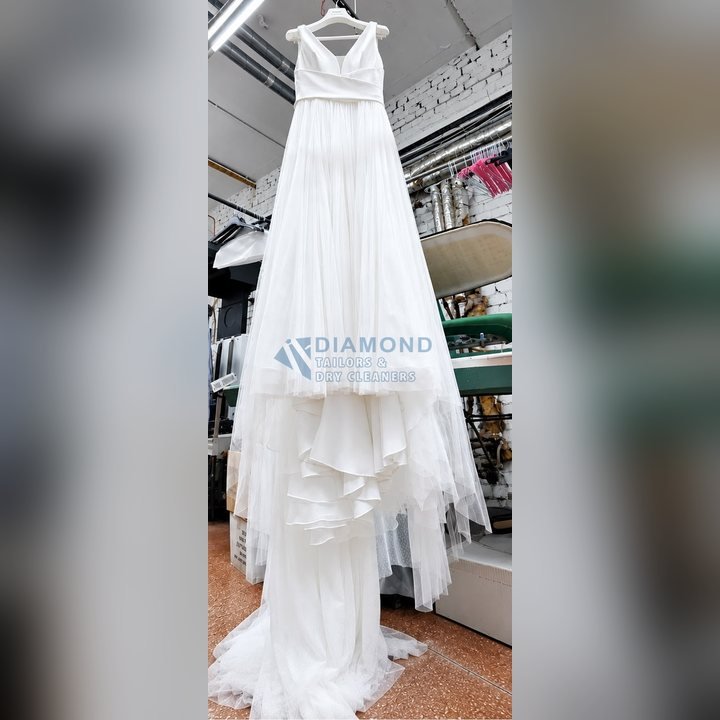 A full-length tulle wedding gown after cleaning, hanging in our workshop