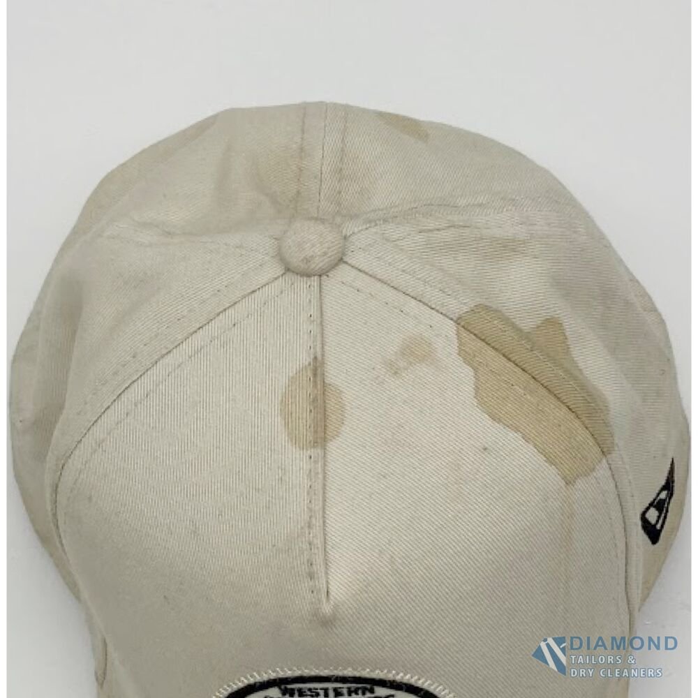 Cream cotton baseball cap before cleaning, with a large brown stain across the crown