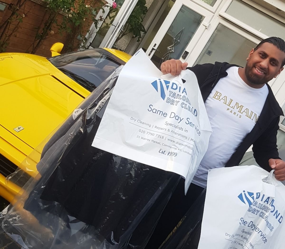 A smiling customer outside his front door holding up his dry cleaning in Diamond Tailors & Dry Cleaners garment bags